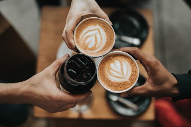 Friends holding ceramic cups of coffee with latte art