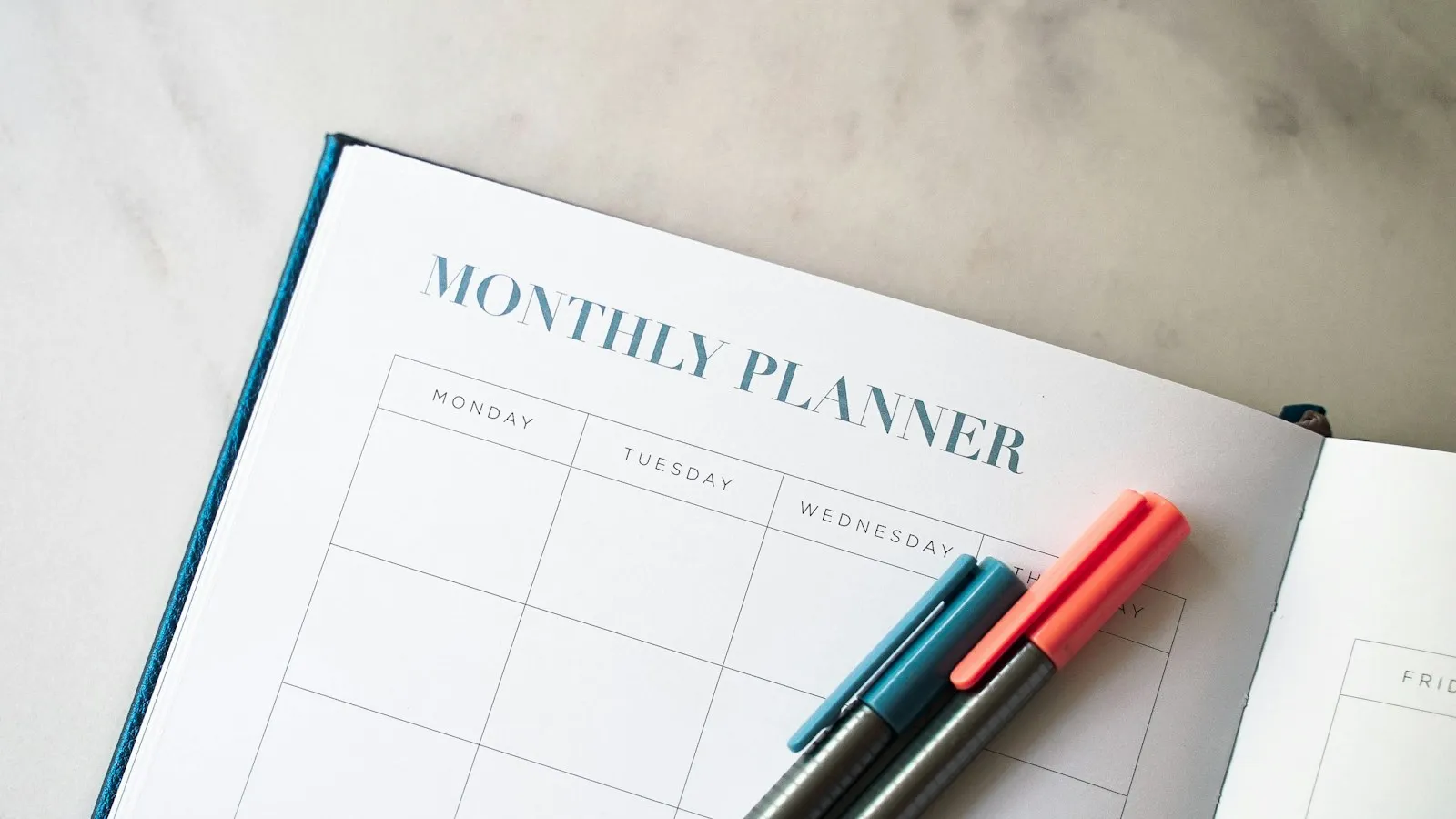 An open printable monthly planner with colored pens on a desk, one of the most popular digital products people find on Pinterest